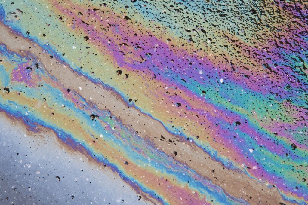 Petrol stain on asphalt road, big polluted puddle water.